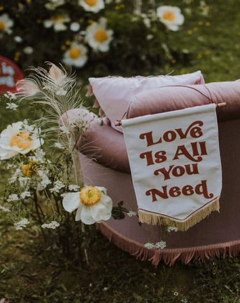Love Is All You Need fabric banner resting on a velvet sofa surrounded by wildflowers for sixties wedding inspiration at a farm