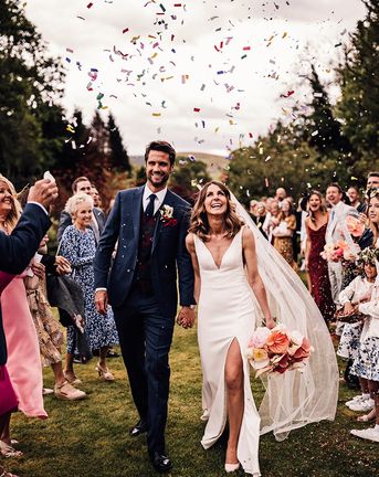 Bride in Suzanne Neville wedding dress with groom in blue suit have confetti exit from outdoor wedding at Rossie On The Earn venue. 