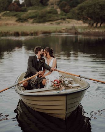 Bride in lace skirt wedding dress rides in boat with groom on the loch at the stunning Cardney Estate wedding venue.