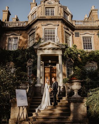The bride and groom walk up the stairs at their wedding venue, Hampton Court House