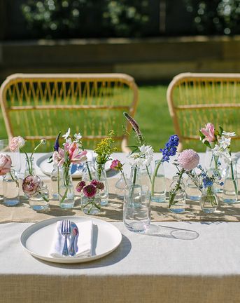 diy wedding centerpiece with mini glass vases and bottles and single stems of brightly coloured spring flowers on a linen tablecloth