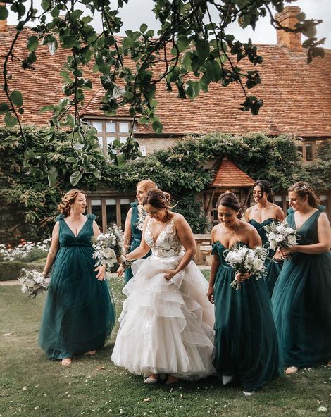 Bride in layered wedding dress walks with bridesmaids in green bridesmaid dresses