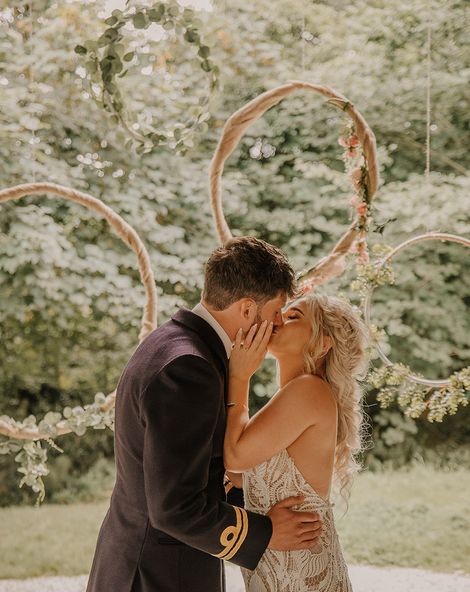 Hula hoop decor for the altar with the bride in a boho lace wedding dress kissing the groom in military uniform. 