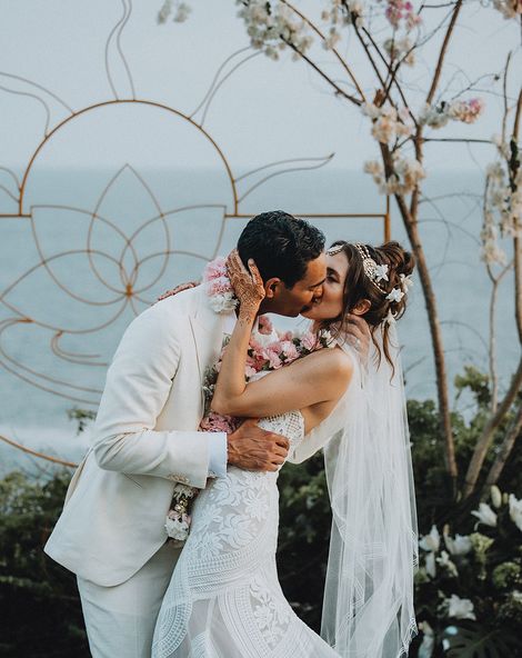 Groom in cream suit kisses bride in boho lace wedding dress and flower hair accessories at Tigre Del Mar wedding in Mexico