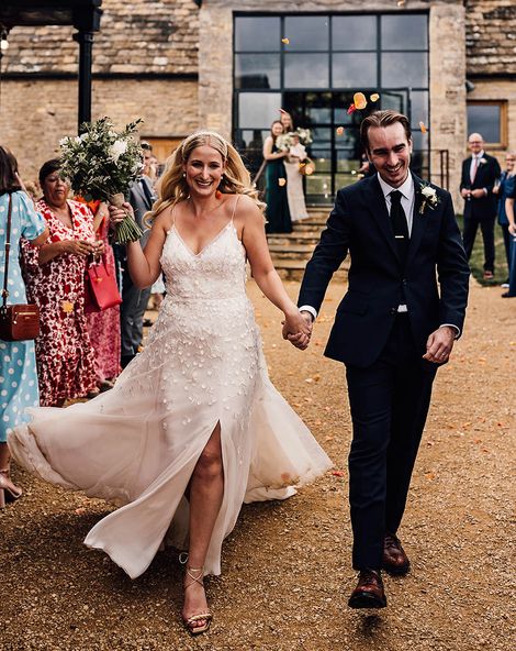 Bride in an Alexandra Grecco Lana wedding dress walking with the groom in a dark blue suit.
