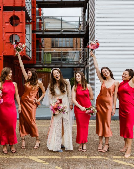 Trinity Buoy Wharf wedding with bride in a lace Rixo dress and bridesmaids in red and orange satin bridesmaid dresses