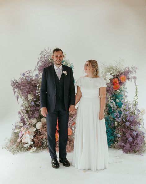 Bride and groom stand holding hands in front of pastel coloured wedding flower columns.
