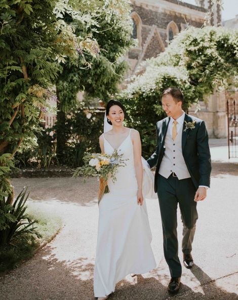 Bride and groom pose together outside their church wedding venue with blue and yellow colour palette as bride wears pearl hair pins and accessories