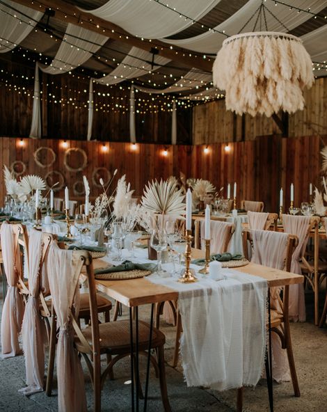 Romantic East Yorkshire Barns wedding reception with pink chiffon chair back decor, pampas grass chandelier, fairy light backdrop and dried palm leaf centrepieces 