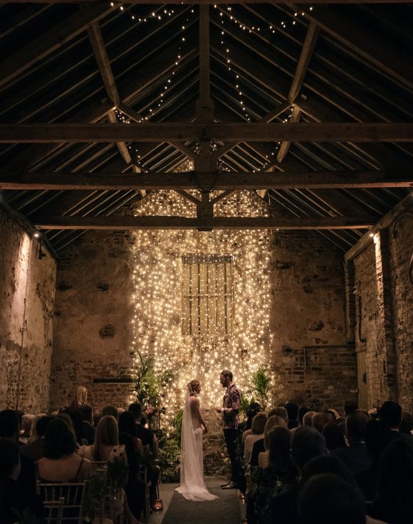 Bride and groom exchange vows in front of cascading fairy lights in The Normans wedding venue Ceremony Barn