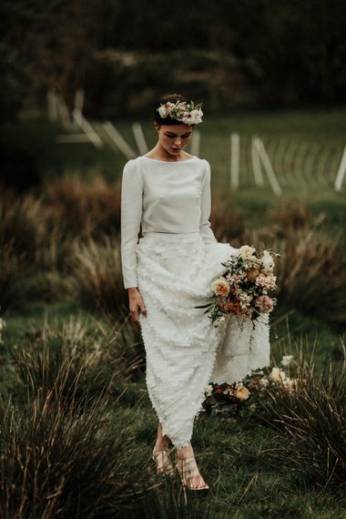 Bride in bridal crop top holding her bouquet and skirt in a field